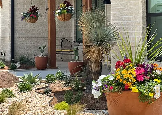 Colorful flower planter and desert landscaping with succulents and yucca in front of a stone patio and porch at a North Texas outdoor living space.