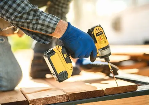 Contractor using a cordless power drill to assemble wooden boards during outdoor construction work.
