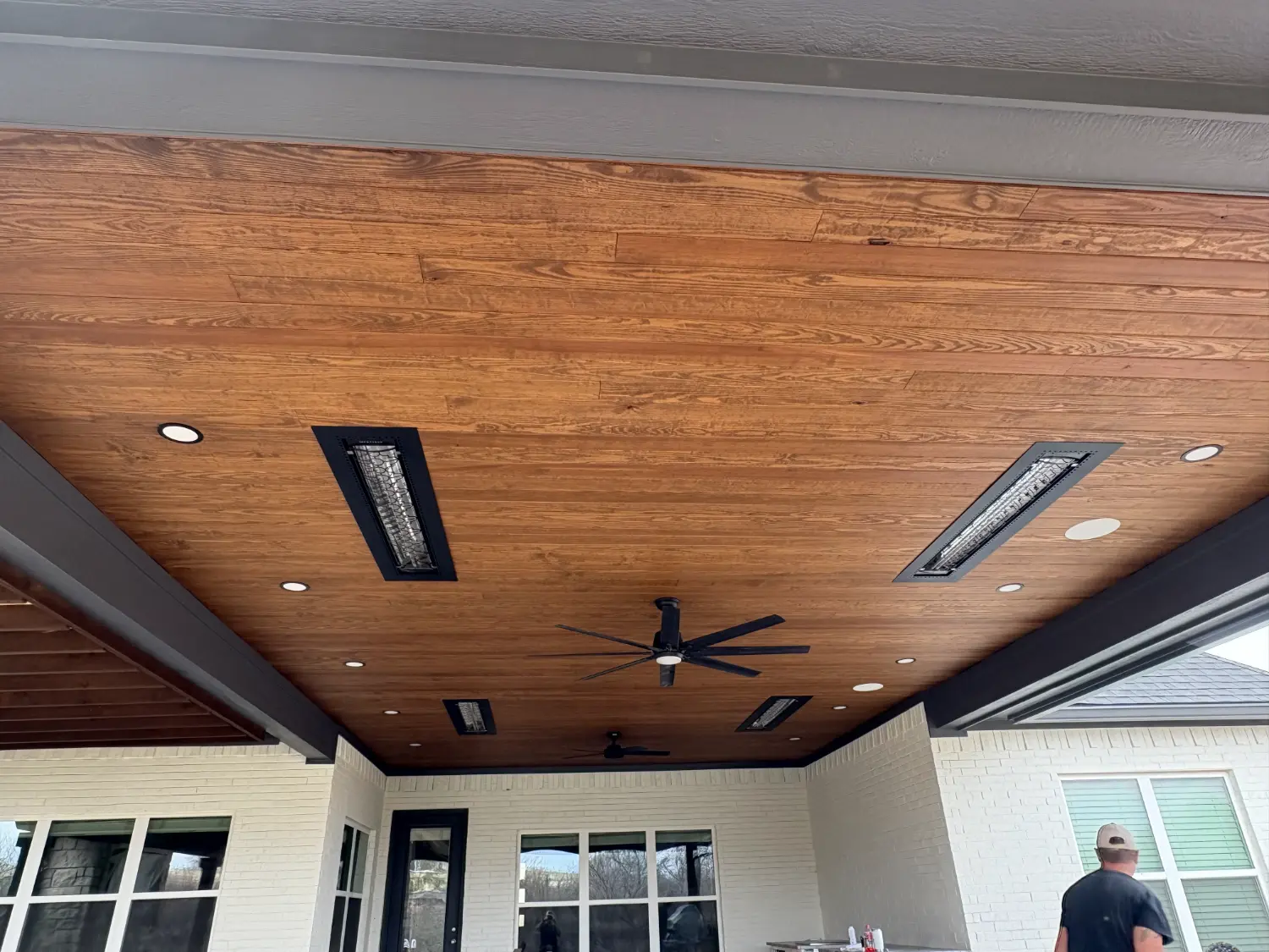 Modern luxury patio ceiling with wood planks, integrated heaters, and ceiling fan for outdoor entertaining