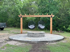 Luxury backyard transformation featuring stone fire pit patio with wooden pergola and hanging egg chairs