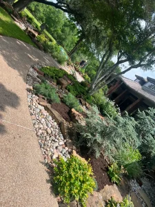 Luxury landscape design featuring tiered stone retaining wall with drought-resistant plants and mature trees