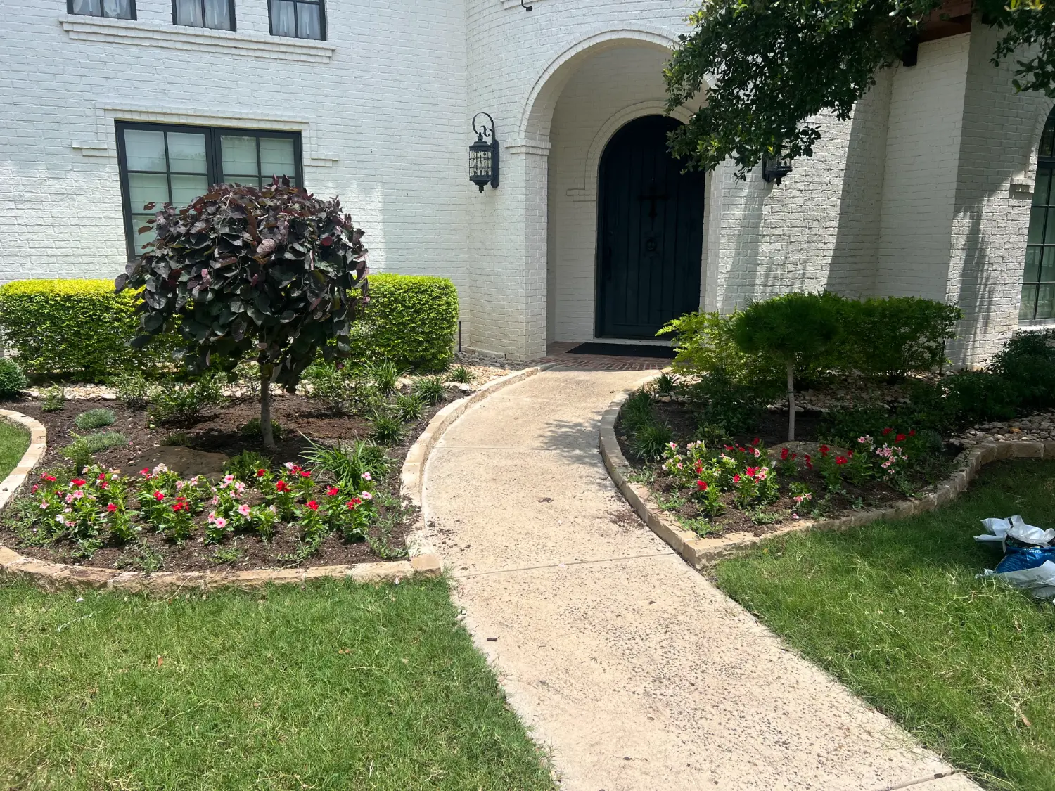 Luxury landscape design with manicured hedges, flowering beds, and curved walkway leading to arched entryway