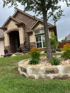 Luxury residential home featuring high-end landscaping with stone tree ring, flowering beds, and manicured lawn