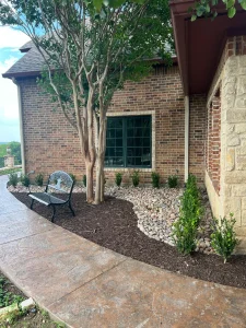 Luxury landscape design featuring multi-trunk tree, decorative stone, and ornamental shrubs near brick home