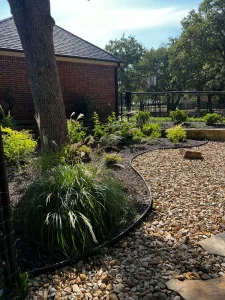Luxury backyard landscape design featuring ornamental grasses, decorative rock pathways, and black metal fencing near brick home
