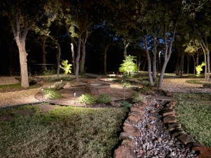 Luxury backyard landscape design featuring fire pit, stone pathways, and uplighting among mature trees in Fort Worth