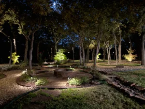 Luxury nighttime backyard with uplighting, fire pit, and mature trees for outdoor entertainment