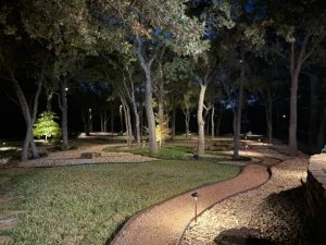 Luxury nighttime backyard with illuminated mature trees, manicured lawn, and winding stone pathway