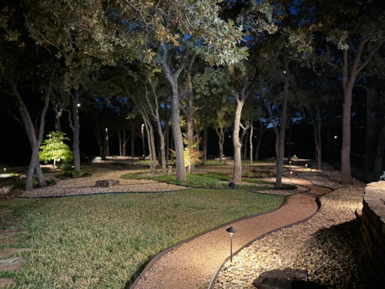 Luxury nighttime backyard with illuminated mature trees, manicured lawn, and winding stone pathway