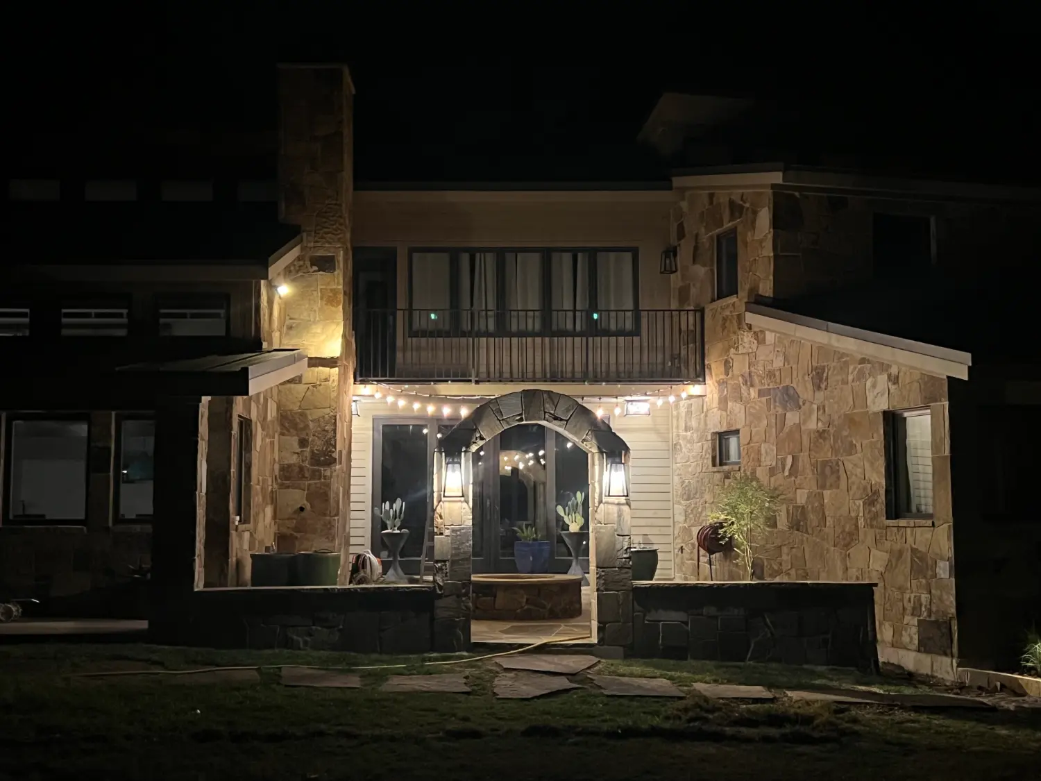 Luxury Fort Worth home's elegant nighttime patio with stone facade and outdoor entertainment lighting
