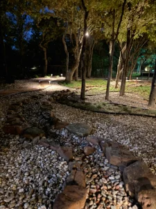 Nighttime luxury landscape design featuring illuminated trees, gravel pathways, and stone features in outdoor living space