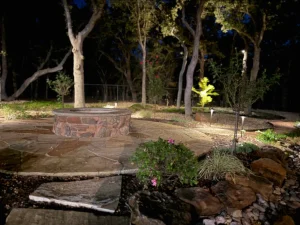 Luxury nighttime backyard transformation featuring illuminated trees, stone fire pit, and custom patio design in Fort Worth