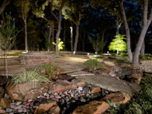 Luxury backyard landscape design featuring illuminated trees, stone pathways, and flowering gardens at night