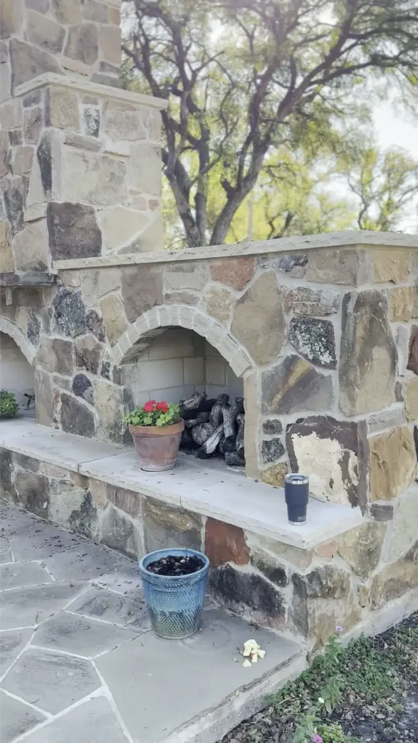Stone outdoor fireplace with arched opening in luxury backyard landscape design