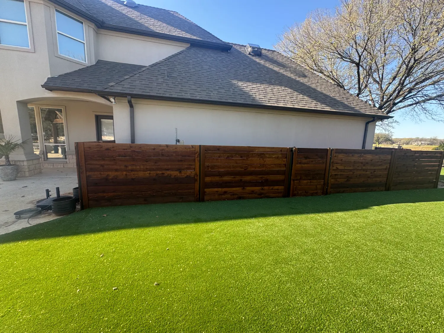 Modern luxury backyard transformation with artificial turf and horizontal wood privacy fence