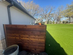 Luxury backyard transformation featuring manicured green lawn, dark wood raised planter, and modern patio design