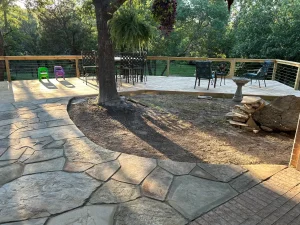 Luxury backyard transformation featuring flagstone patio, wooden deck, and entertainment area surrounded by mature trees
